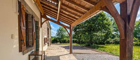 A covered outdoor area with stone flooring, wooden beams, and a stone building with windows.