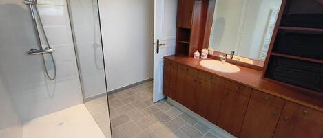 Een moderne badkamer met een glazen douchecabine, een houten wastafelmeubel met een wastafel en een grote spiegel erboven.