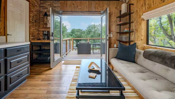 Een houten interieur met een bank, salontafel en openslaande deuren naar een balkon met uitzicht.