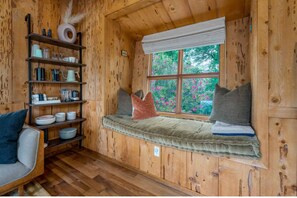 Ein Holzhütten-Interieur mit einer eingebauten Bank an einem Fenster, Regalen mit Küchenutensilien und einem Holzboden.