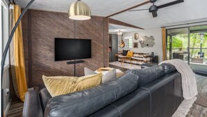 A modern living room with a leather sofa, a flat-screen TV, a ceiling fan, and a large window. - Creekside retreat + hot tub near Sedona (Cornville)