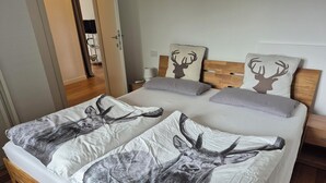 A bed with a deer print bedspread, a wooden headboard, and two pillows with deer prints. - Apartment Sunshine lake and mountain view with 60 sqm terrace facing south and east (Millstatt)