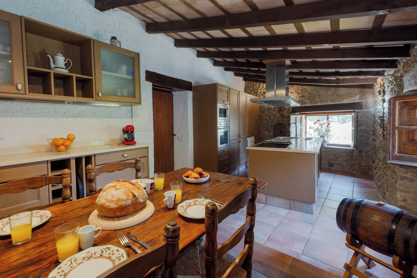 Une cuisine rustique avec une table en bois mise pour le petit-déjeuner, comprenant du pain, des fruits et du jus.