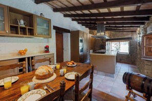 A rustic kitchen with a wooden table set for breakfast, including bread, fruit, and juice.