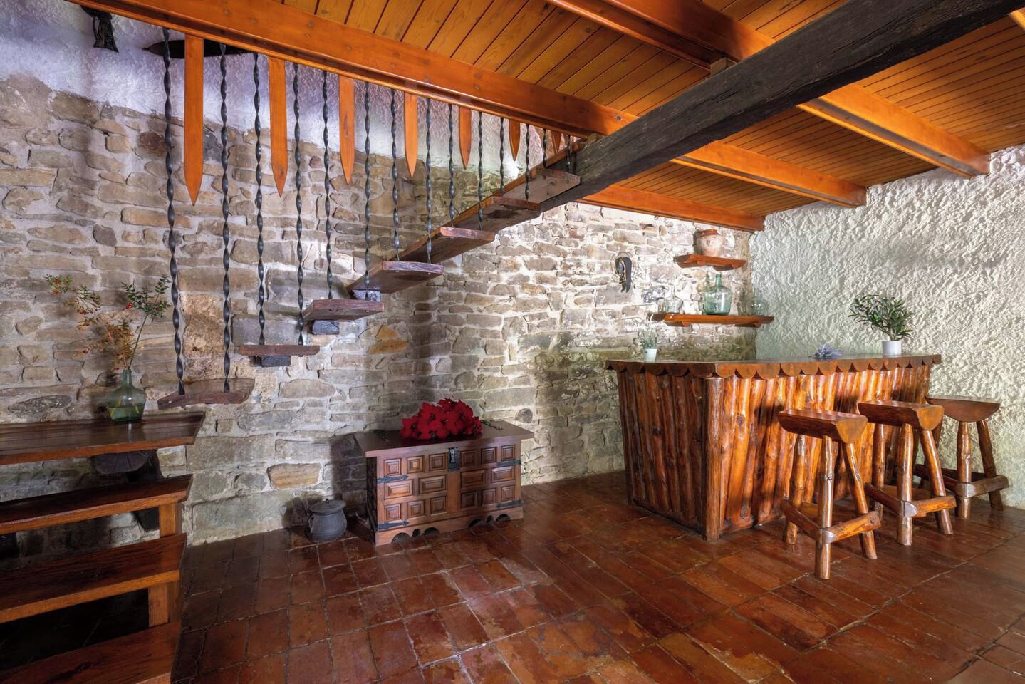 Un interior rústic amb una paret de pedra, una escala de fusta, zona de bar i un arca de fusta.