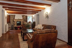 Ein gemütliches Wohnzimmer mit Kamin, Ledersofa und Holzbalken an der Decke.