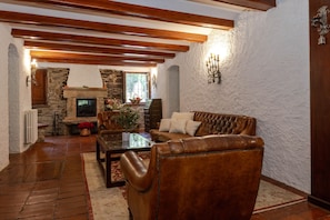 A cozy living room with a stone fireplace, leather sofa, wooden beams, and a stone wall. - Garrotxa Nature House by Fidalsa , (Les Planes d'Hostoles)
