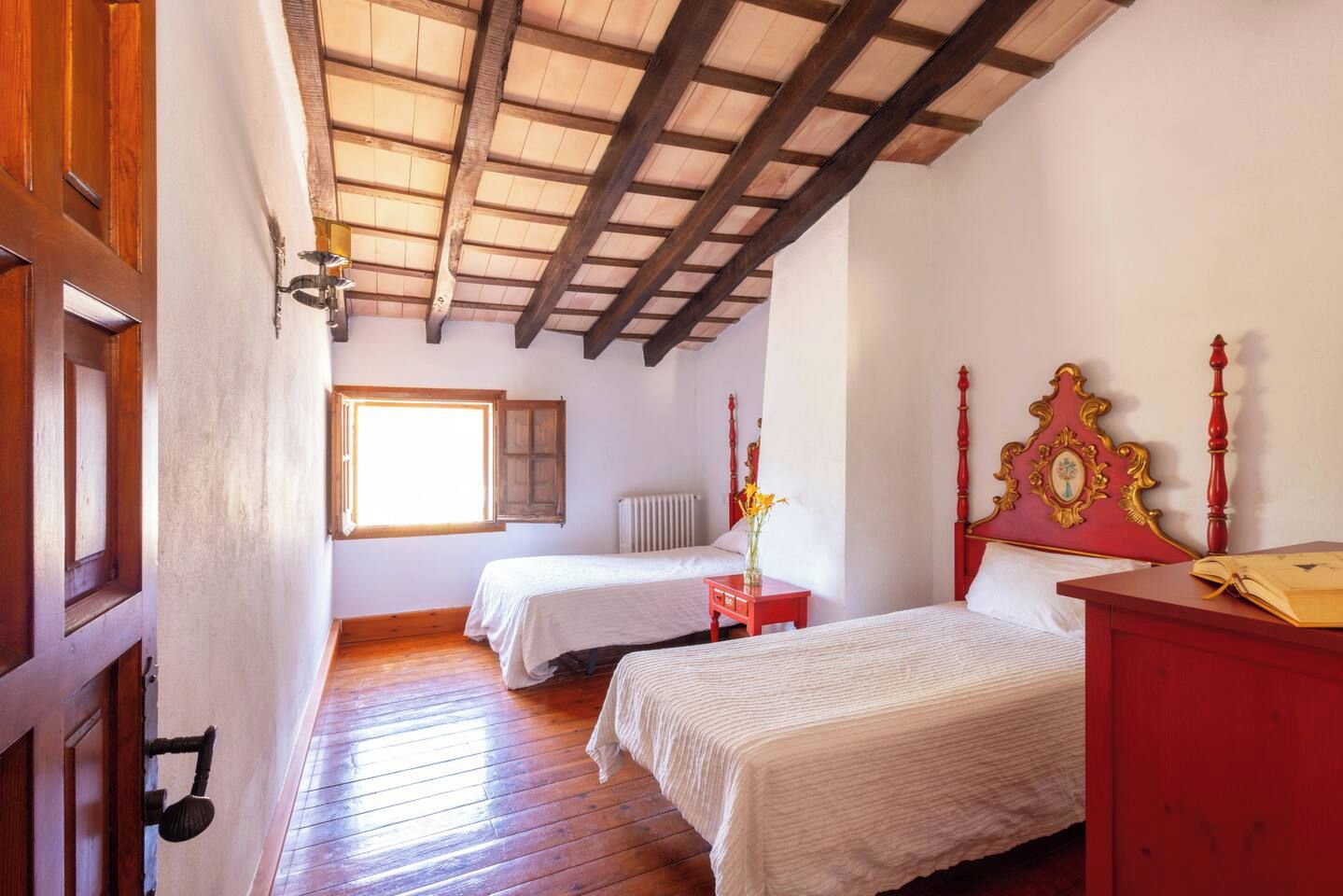 Un dormitorio con dos camas, suelo de madera, techo inclinado con vigas a la vista, una ventana y un radiador.