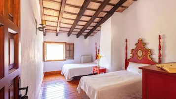 Une chambre avec deux lits, un plancher en bois, un plafond en pente avec des poutres apparentes, une fenêtre et un radiateur.