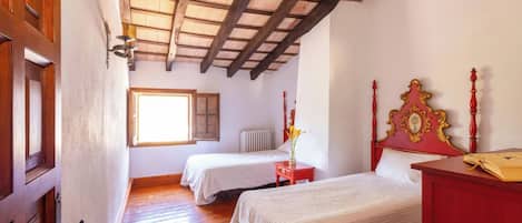 Quarto com duas camas, piso de madeira, teto inclinado com vigas aparentes, janela e radiador.