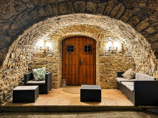 A stone-walled room with a wooden door, two wall-mounted lights, a sofa, and two side tables.