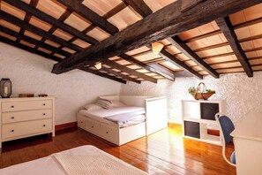 Une chambre avec un plafond en pente, des poutres en bois, un lit, une commode, une chaise et une petite table sur laquelle se trouve un panier.