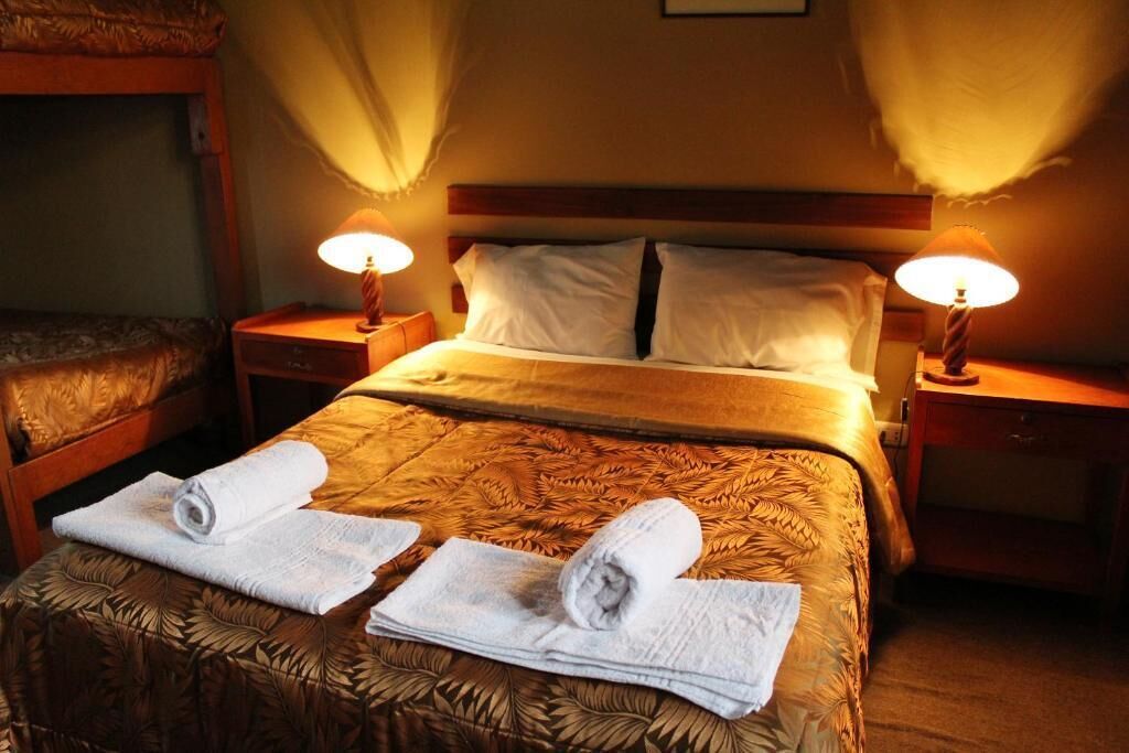 A hotel room with a bed, two bedside lamps, a nightstand, and a rolled towel on the bed.