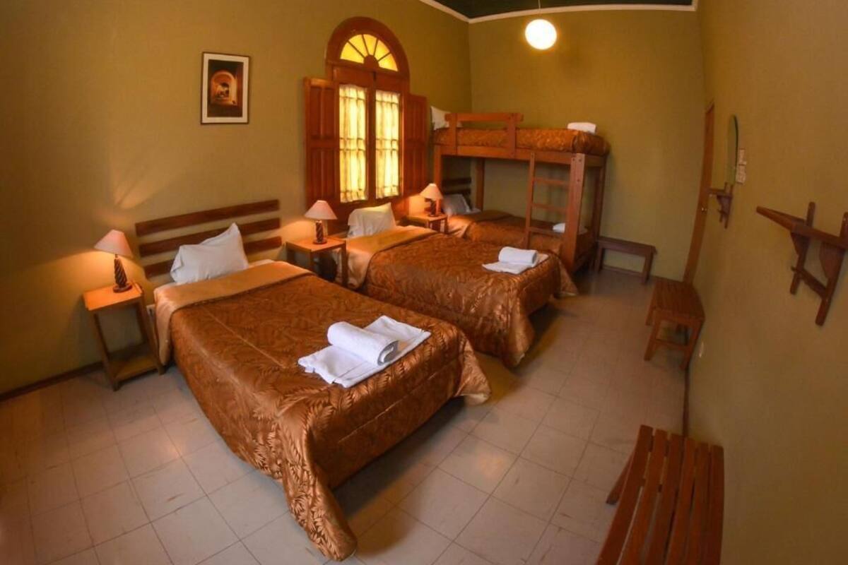 Habitación de hotel con dos camas, un banco de madera, una mesita y un estante en la pared.