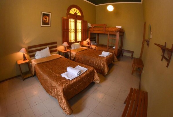 A hotel room with two beds, a wooden bench, a small table, and a wall-mounted shelf.