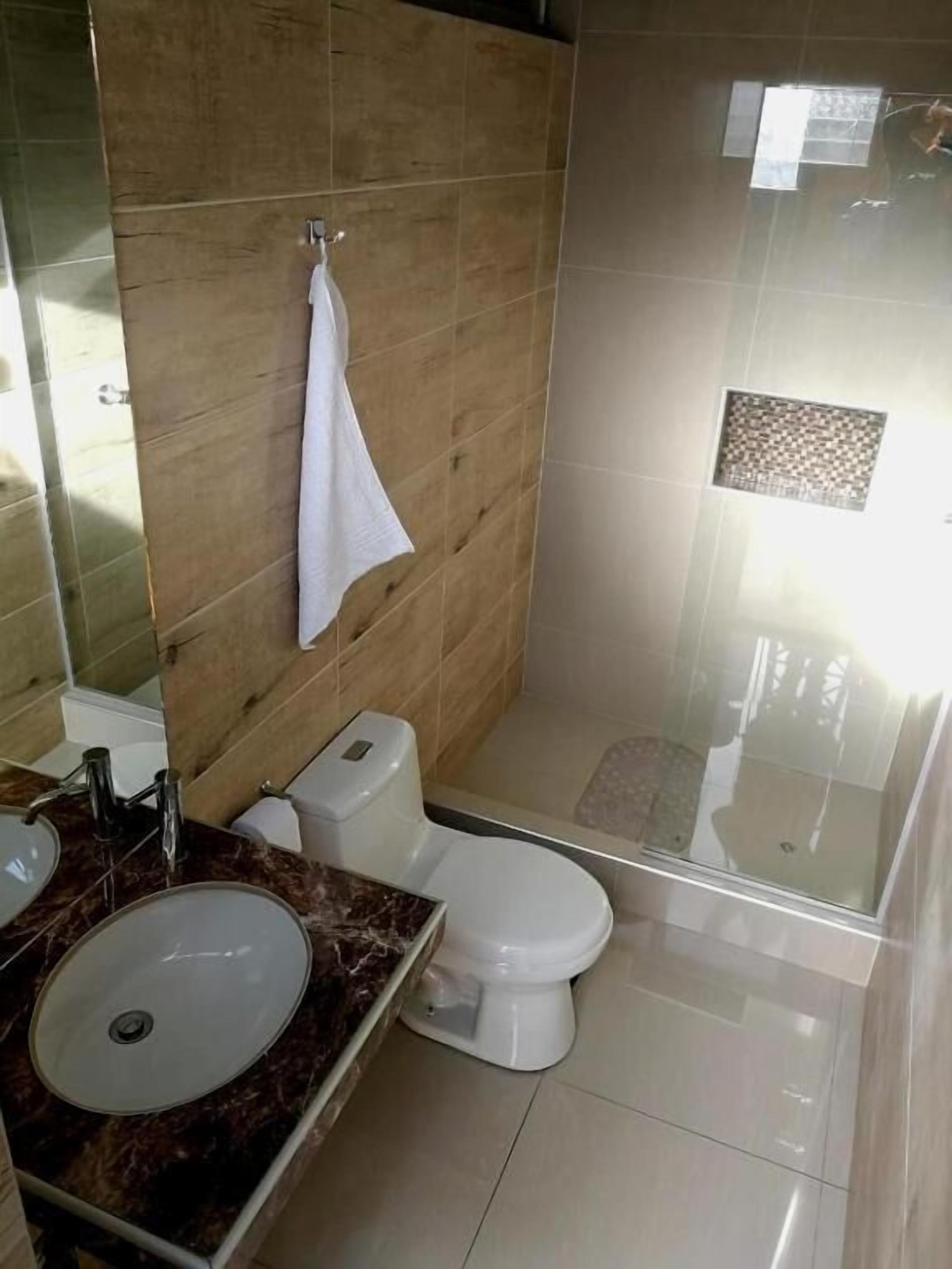 Un baño con lavamanos, inodoro y cabina de ducha con mampara de vidrio.