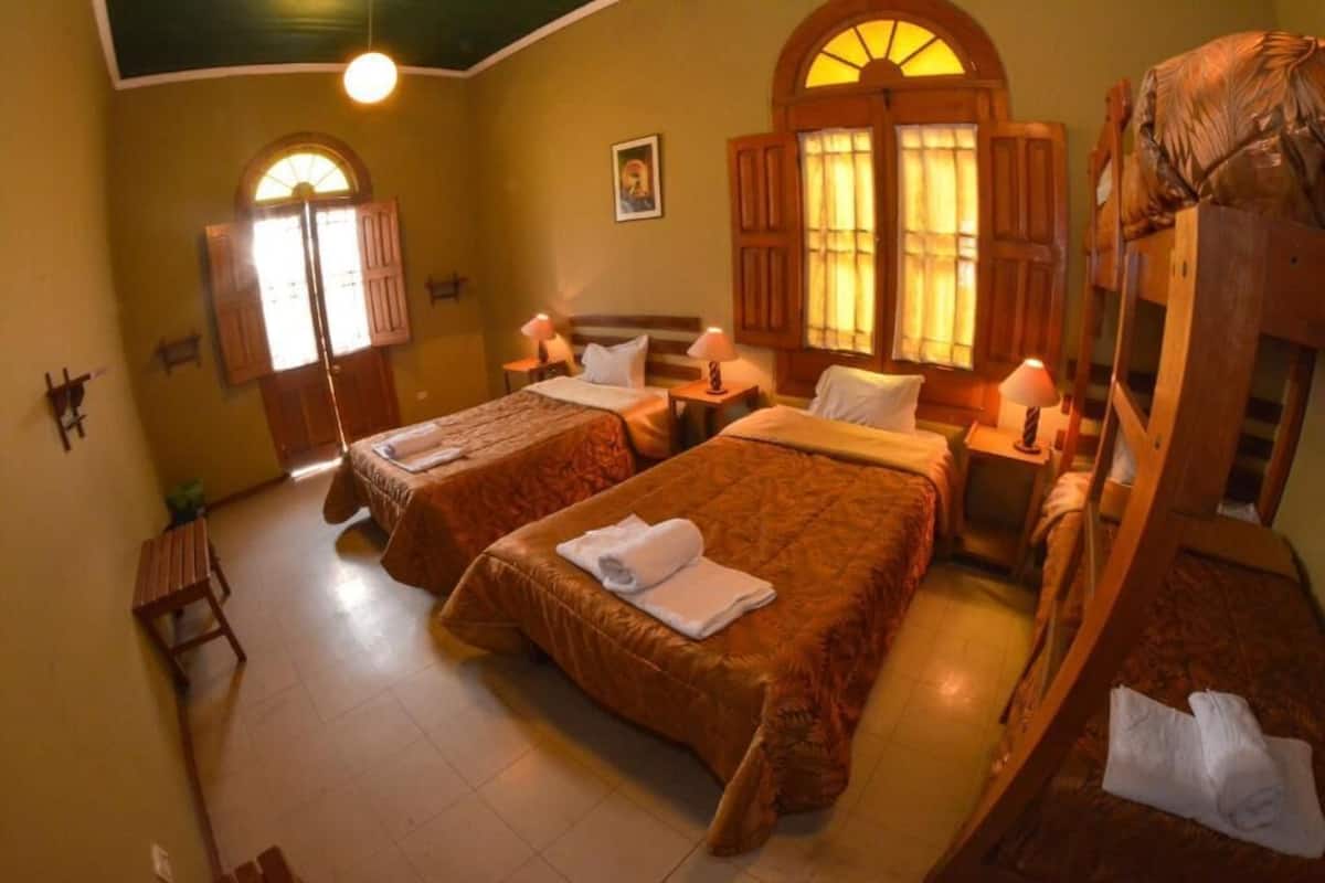 Una habitación de hotel con dos camas, muebles de madera y un gran ventanal con cortinas.