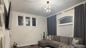 Uma sala de estar com sofá seccional, uma TV de tela plana fixada na parede, parede decorativa com espelhos circulares e luminária no teto.