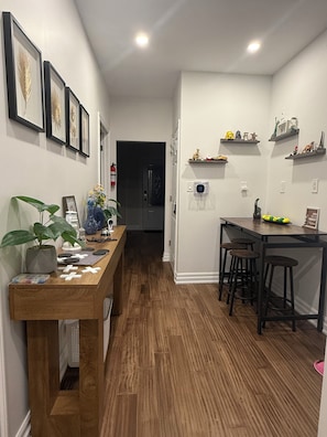 Un couloir avec une table en bois, des chaises, une plante en pot et des tableaux encadrés accrochés au mur.