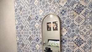 Quarto com parede estampada, cama com colcha cinza, espelho e duas quadros emoldurados.