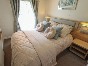 A neatly made bed with a quilted cover, two pillows, and a bedside table with a lamp. - P and M Luxury Lodge Br15 (Lincoln)