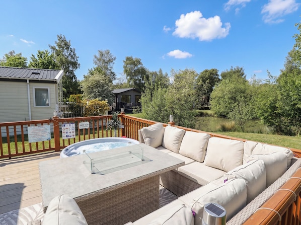 A hot tub on a deck with a wicker sofa and a glass table. - P and M Luxury Lodge Br15 (Lincoln)