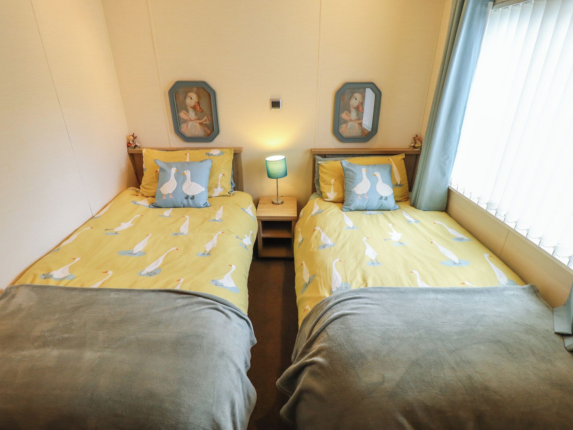 A twin room with two beds, each with goose-patterned bedding, a nightstand with a lamp, and two wall-mounted mirrors.