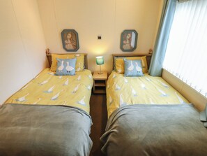 Ein Doppelzimmer mit zwei Betten, jedes mit Gänsenmuster-Bettwäsche, einem Nachttisch mit Lampe und zwei Wandspiegeln.