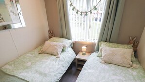 Una habitación con dos camas, una mesita de noche con lámpara y una ventana con cortinas.
