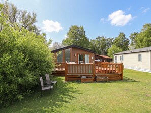 A mobile home with a deck, a small porch, and a lawn area with a chair and table.