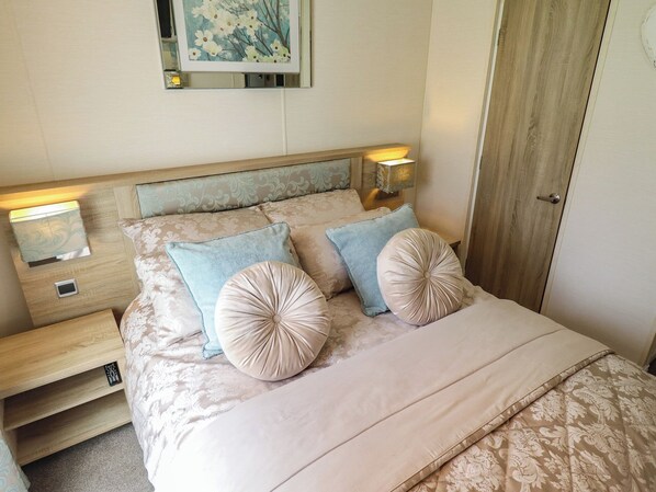 A neatly made bed with a headboard, two bedside tables, and a wall-mounted lamp.