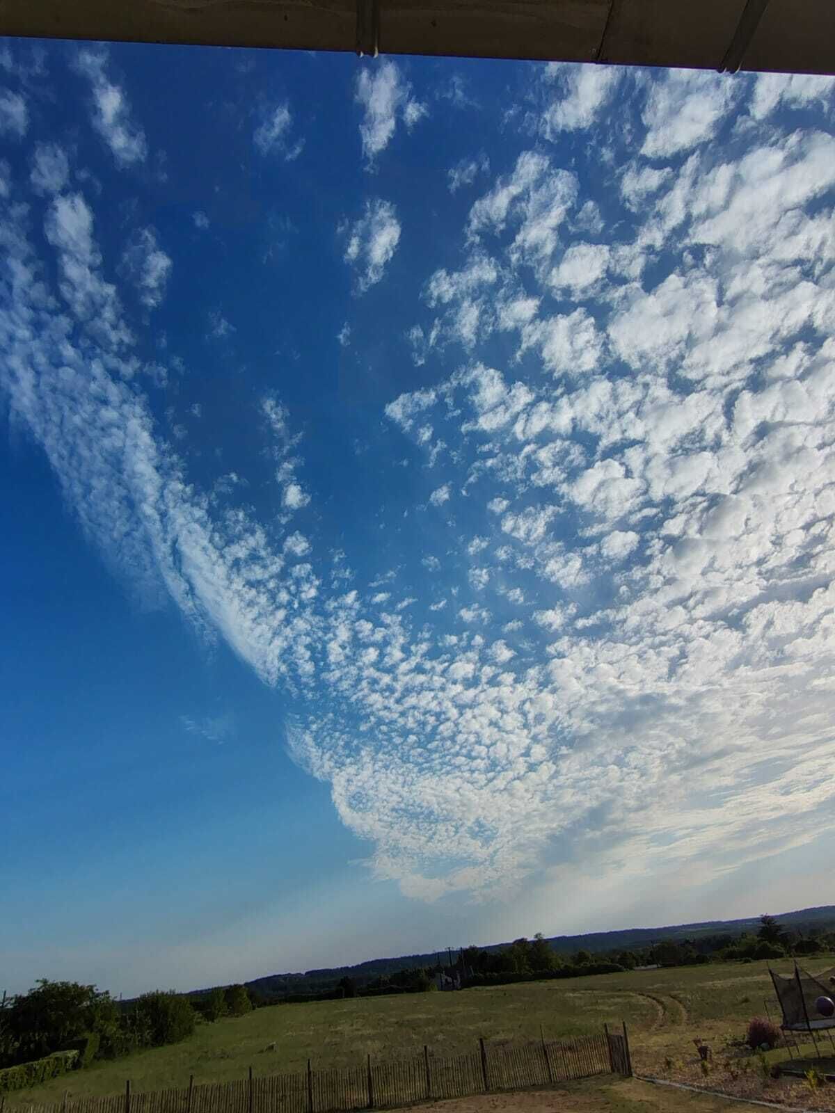 Een heldere lucht met enkele wolken boven een landelijk gebied.