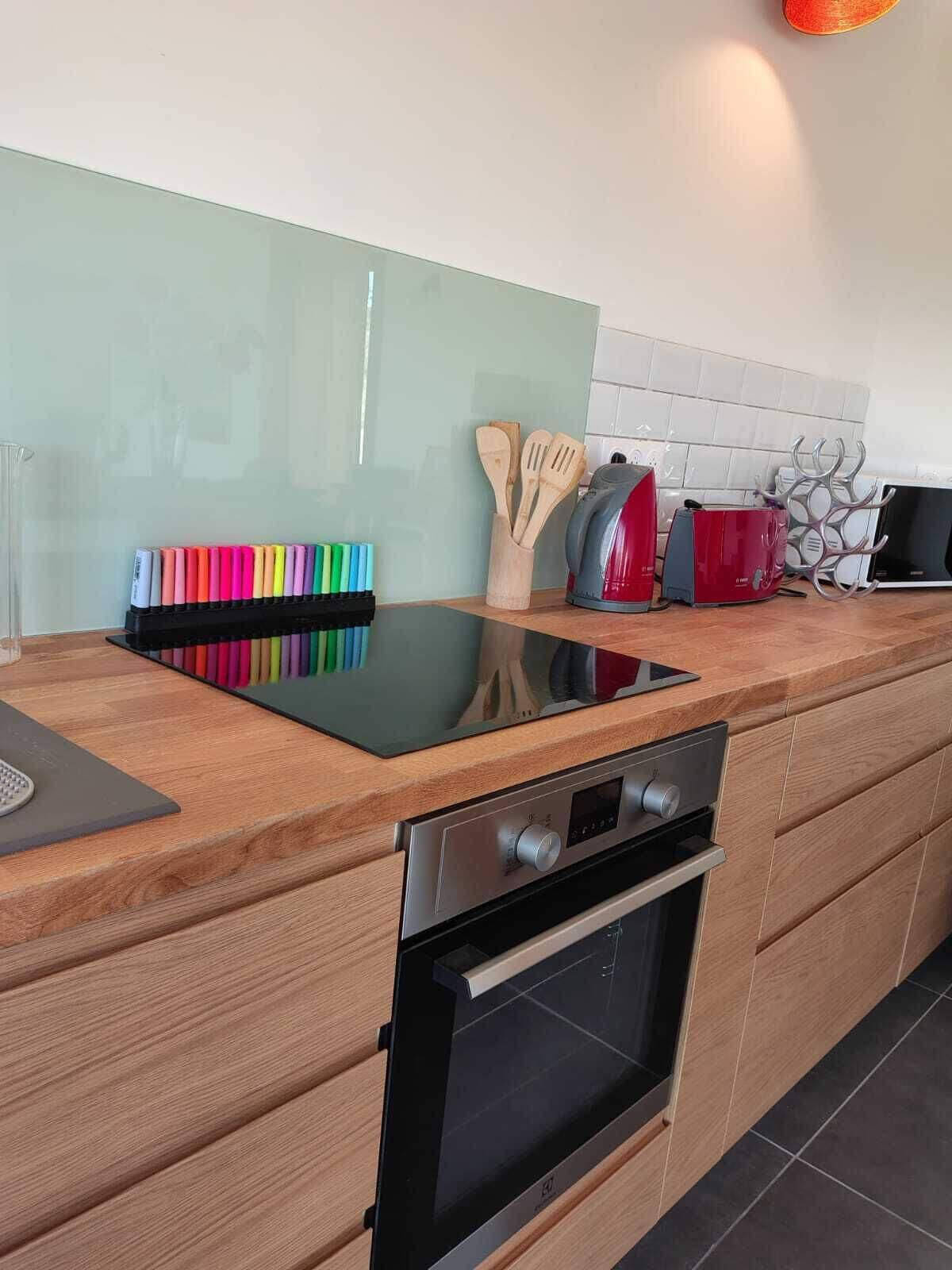 A modern kitchen with a black induction cooktop, stainless steel oven, wooden cabinets, and a glass backsplash.