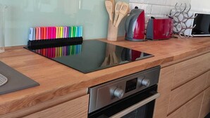 A modern kitchen with a black induction cooktop, stainless steel oven, wooden cabinets, and a glass backsplash. - New house in the heart of the Loire castles - sleeps 4 (Chinon)