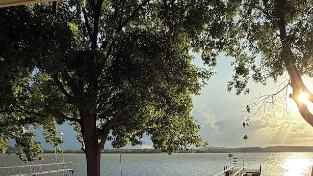 A lakeside patio with metal chairs and a table, a tree, and a dock extending into the water. - Swim Platform + Lakefront Double Deck + Walk to Marina + Near Rocker B (Graford)