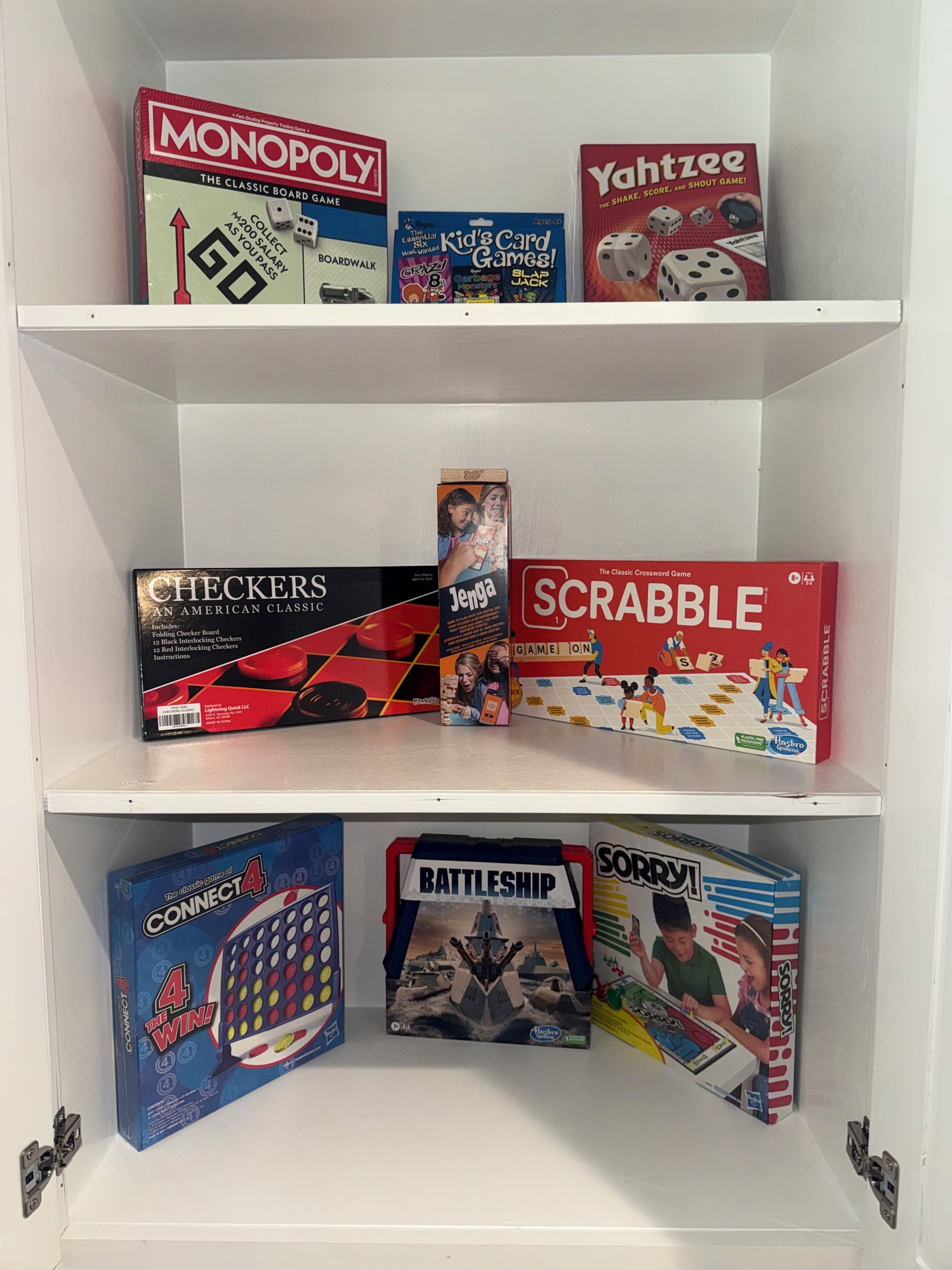A shelf with various board games including Monopoly, Scrabble, Checkers, Connect 4, Battleship, and Yahtzee.