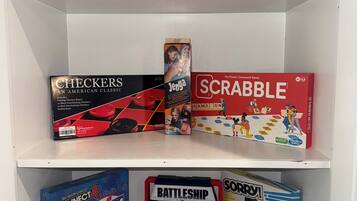 A shelf with various board games including Monopoly, Scrabble, Checkers, Connect 4, Battleship, and Yahtzee.