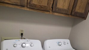 Een wasruimte met twee witte wasmachines voor inlaad, houten kastjes erboven en een stopcontact aan de muur.
