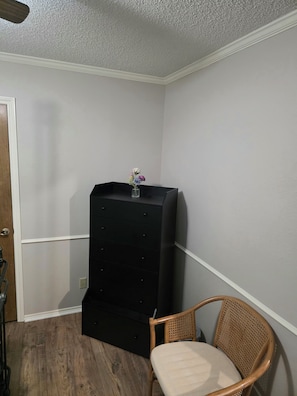 Ein Eckzimmer mit einer schwarzen Unterhaltungsanlage, einem Korbstuhl und einer kleinen Vase mit Blumen.