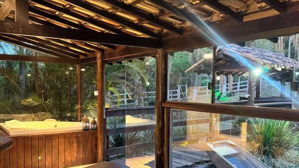 A room with a hot tub, wooden flooring, and large windows overlooking a garden.
