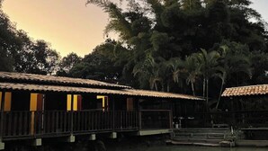 A row of wooden cabins with a water body in the foreground, surrounded by dense foliage.