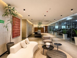 Eine moderne Lobby mit einer Couch, Sesseln, einem Empfangstresen und einer Glaswand, durch die Autos zu sehen sind.