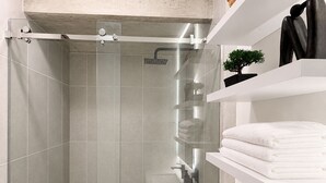 Een moderne badkamer met een douchecabine van glas, witte betegelde wanden en een witte plank met handdoeken en een bloempot.