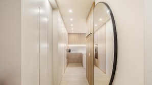 A modern hallway with a large mirror, wooden cabinets, and a kitchenette area. - Golden Dunes Apartment by Minho s Guest (Esposende)