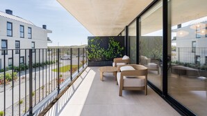 Un balcón con mobiliario exterior, vistas a la calle, y un edificio con pared de azulejos y plantas.