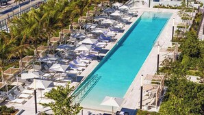 Una lunga piscina con lettini e ombrelloni, immersa nel verde e sotto un cielo sereno.