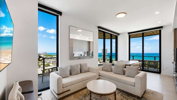 Un soggiorno moderno con una grande finestra vista spiaggia, un divano, un tavolino da caffè e un arredamento minimalista.