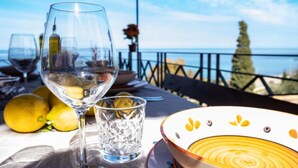 A table with a wine glass, a glass of water, lemons, and a plate with a yellow design. - Sea Pool and Relax Cefalù (Cefalù)