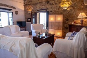 Una sala de estar acogedora con muebles blancos, una pared de piedra y un televisor.