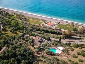 Vista aérea de una propiedad costera con piscina, un edificio de techo rojo y una playa.